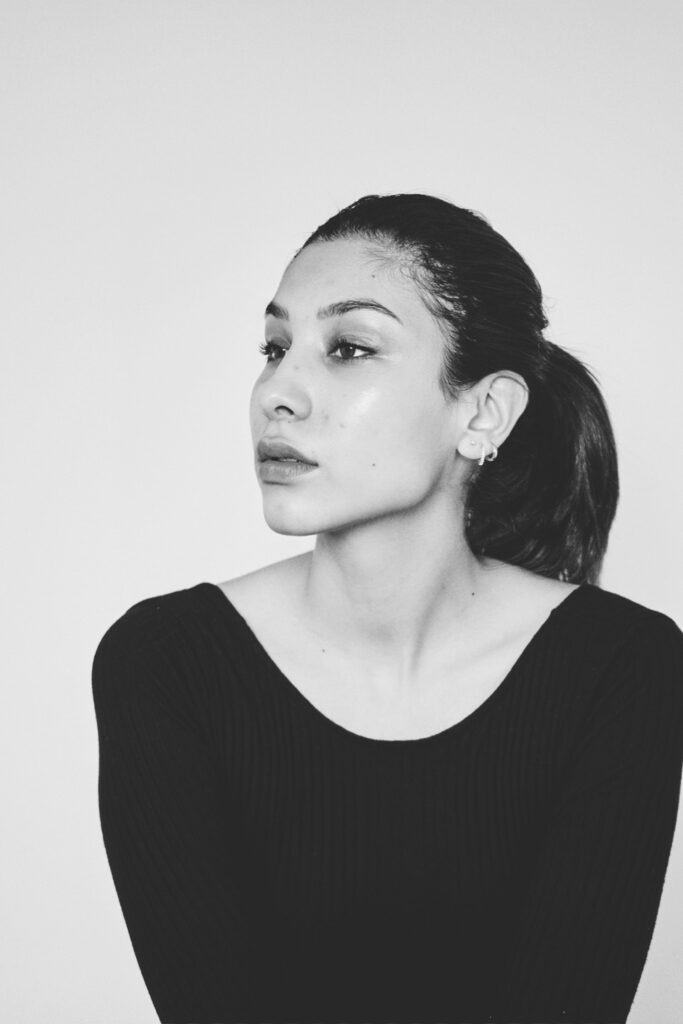 Nadya Inzunza is shown in a black and white portrait gazing to her right with a neutral expression. She wears a black top and has a small earring in her left ear.